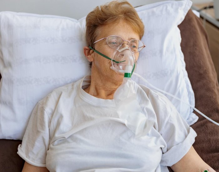 Senior female patient in a breathing mask lies in the ward during treatment for Covid-19